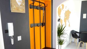 Ein Zimmer mit einer dunklen Wand, einem Holzschild, einem Metallregal, einer Topfpflanze und einem Paar Hausschuhen.