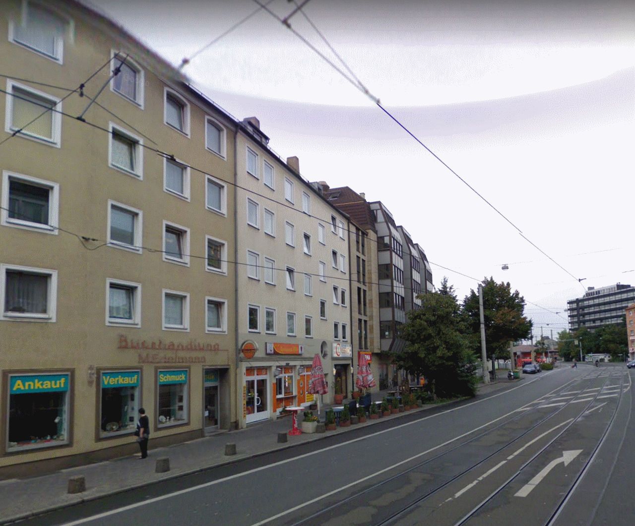 A street with multi-story buildings, shops, and a tram line.