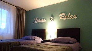 Ein Hotelzimmer mit zwei Betten, einem Wandzeichen mit der Aufschrift "Dream & Relax" und einem Fenster mit Vorhängen.