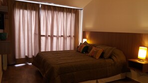 A hotel room with a large bed, a bedside lamp, and a window with curtains.