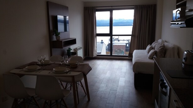 A compact living space with a dining area, a sofa, and a view of a body of water through large windows. - Bariloche Downtown 3 II (San Carlos de Bariloche)