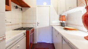 A narrow kitchen with white cabinets, a red stove, and a window above the sink. - Campo Home (Rome)