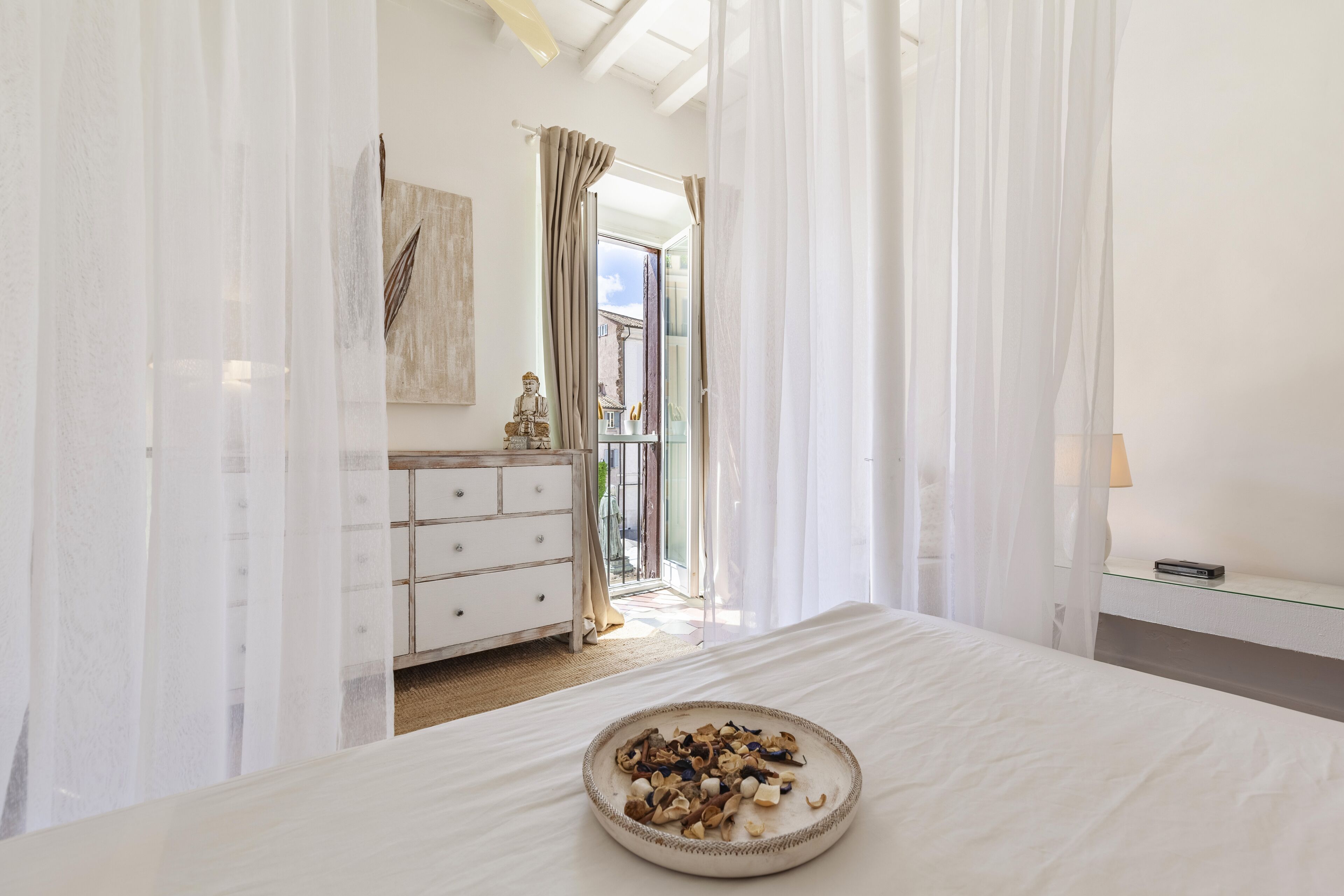 A bedroom with a bed, a dresser, a lamp, and a view of the outside.