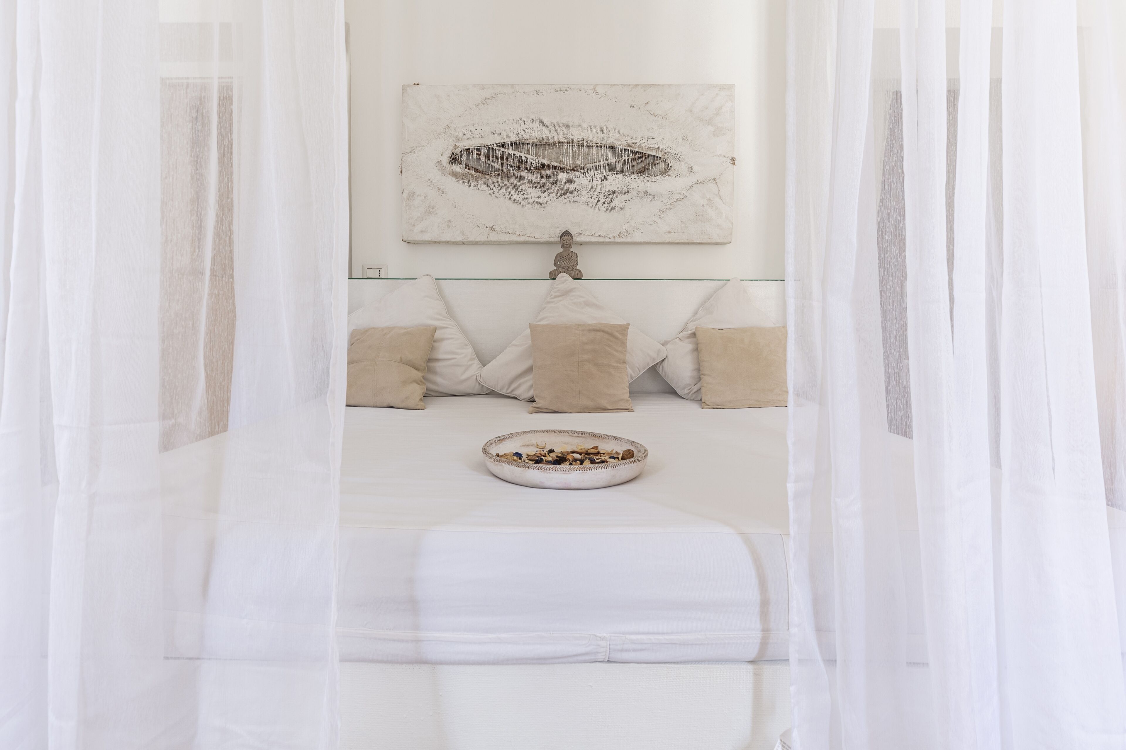 A bedroom with a bed, a wall-mounted artwork, and a bedside table with a bowl of fruit.
