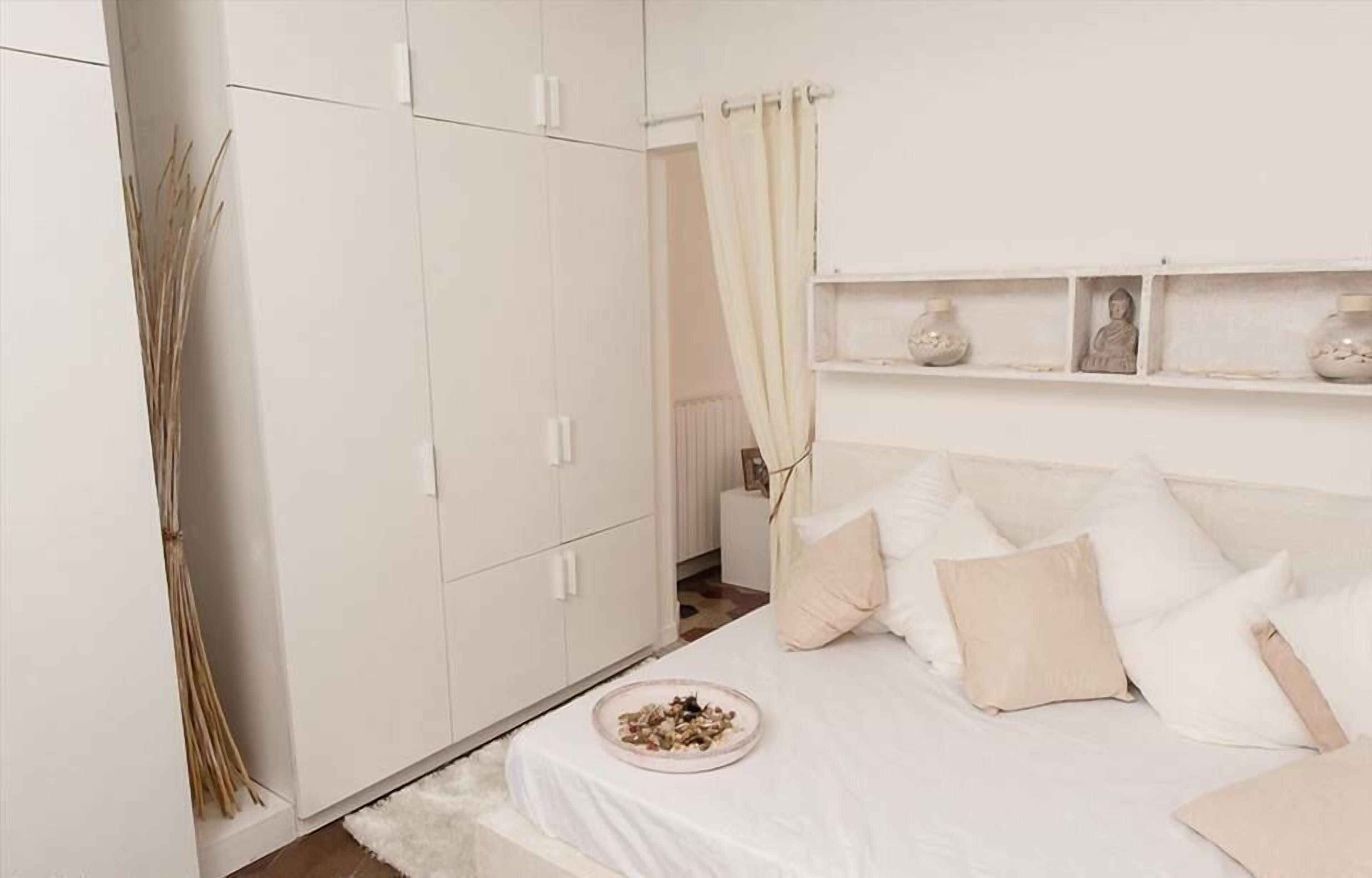 Un dormitorio con cama, armario blanco y estante con adornos.