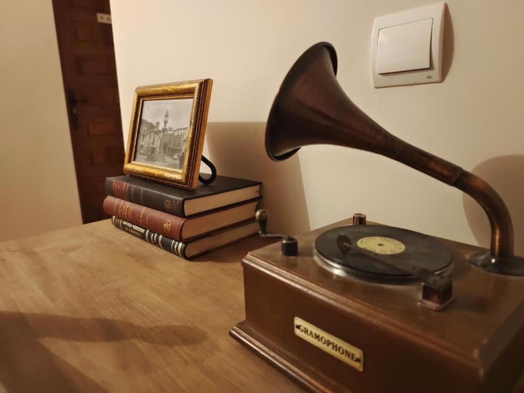 A gramophone on a wooden table with books and a framed picture beside it.