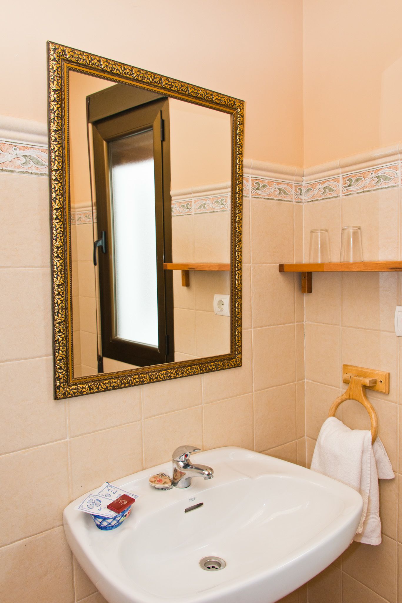 Une salle de bain avec un lavabo blanc, un miroir doté d’un cadre doré orné et un porte-serviettes.