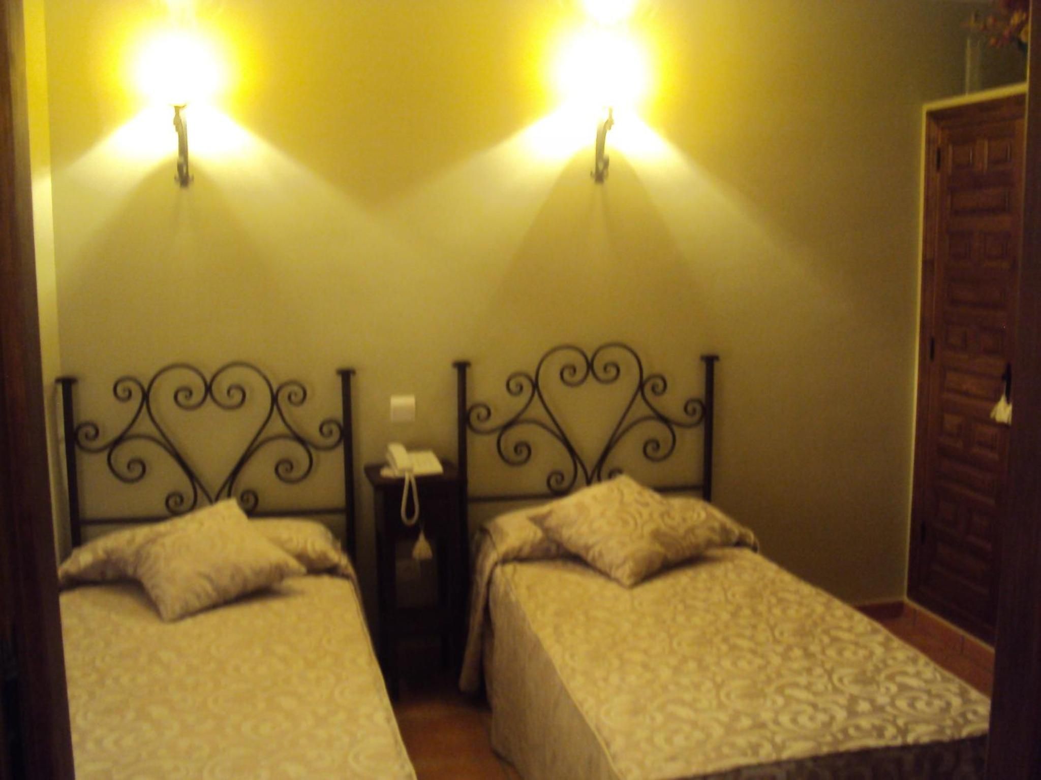 Una habitación con dos camas individuales, una mesita de noche con lámpara y una puerta de madera.