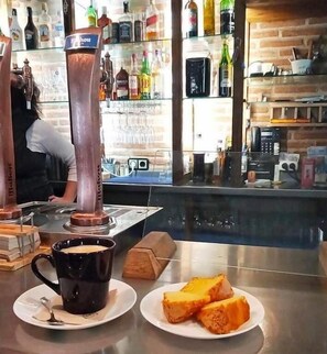 Angolo bar con una macchina da caffè, un ripiano in vetro con bottiglie e un piatto con fette di pane tostato.