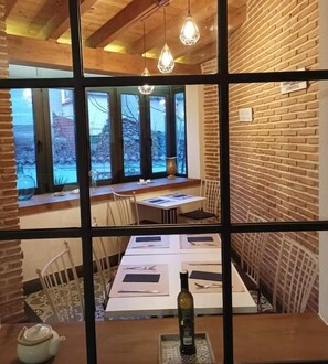 Un'area pranzo con parete in mattoni, soffitto in legno e lampade a sospensione. I tavoli sono apparecchiati con sottopiatti e posate.