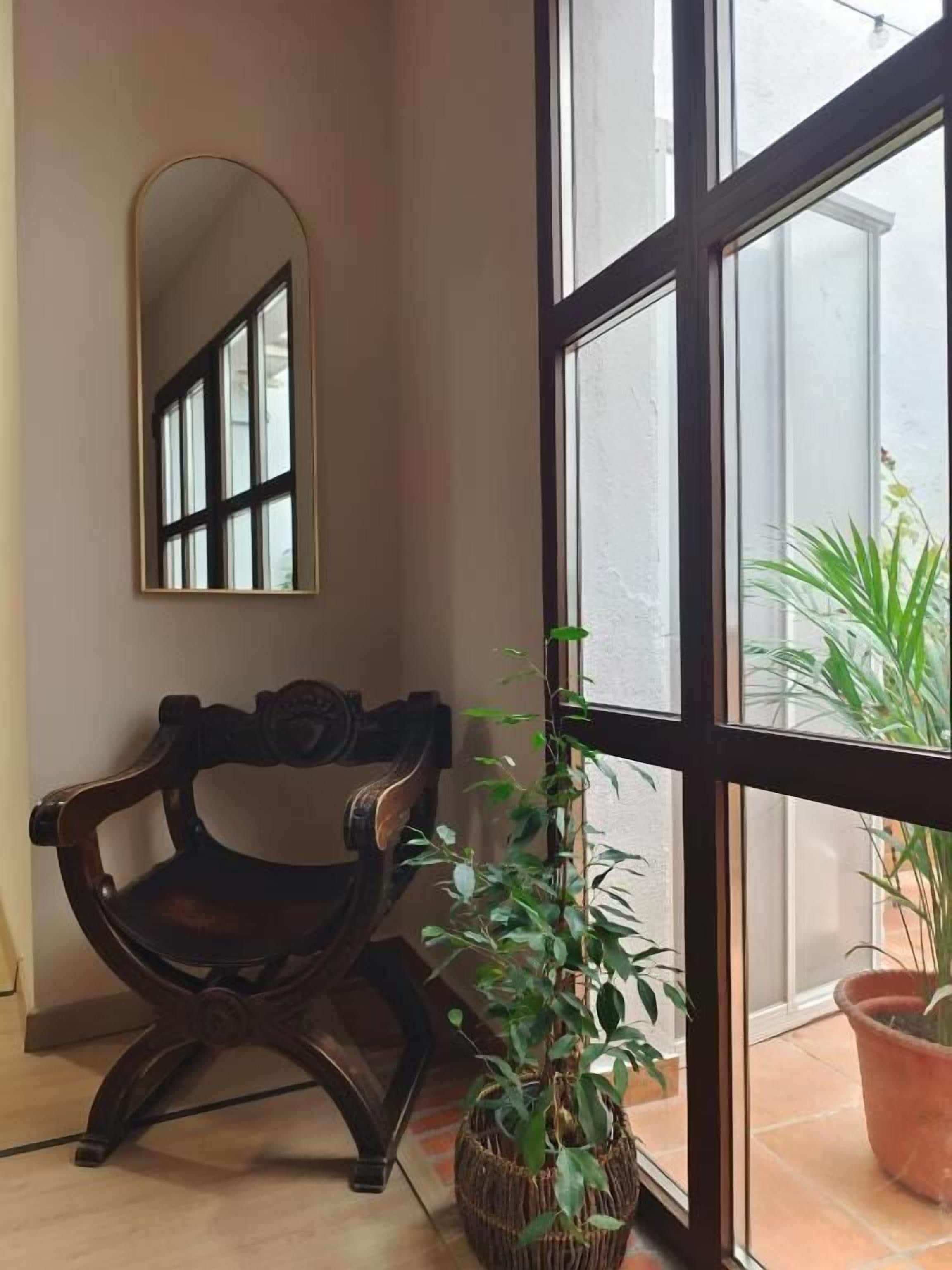 A room with a large window, a mirror, a wooden chair, and a potted plant.