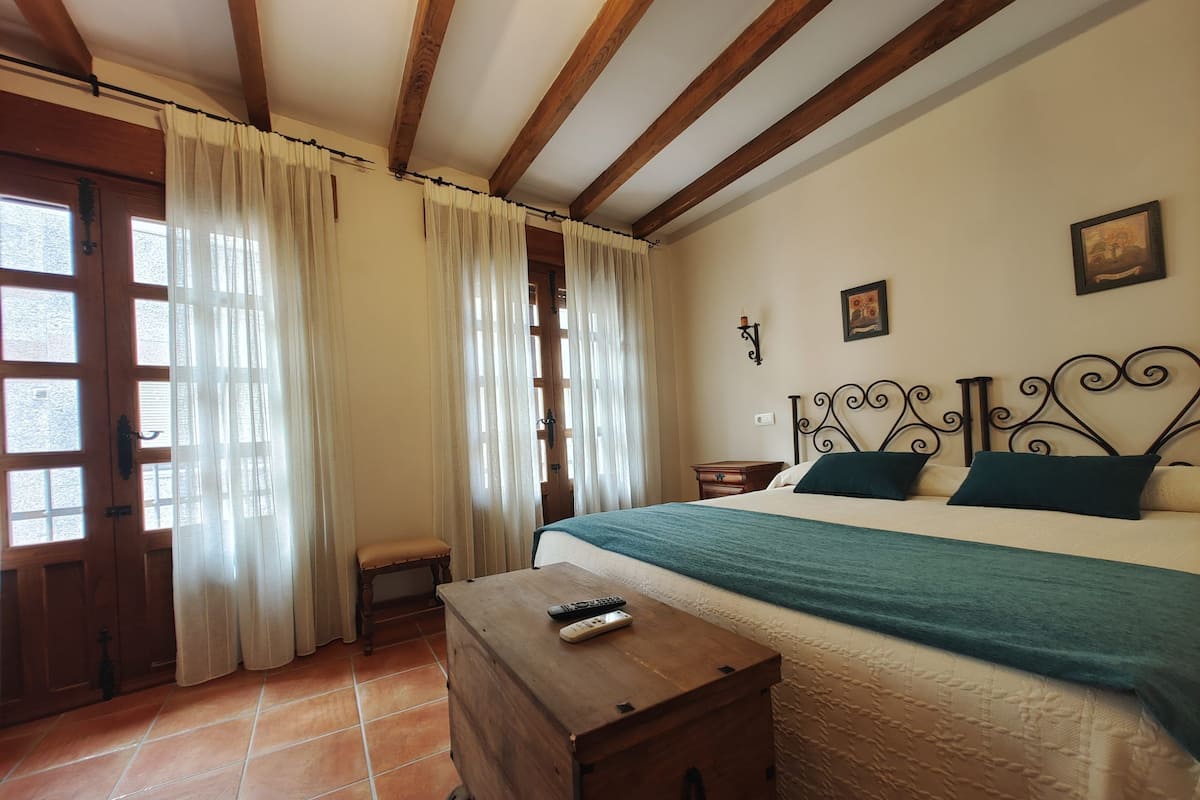 A bedroom with a wooden bed, a nightstand, a bench, and a window with curtains.