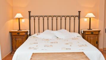 A neatly made bed with a patterned bedspread, two bedside tables with lamps, and a wooden bench in front of the bed.