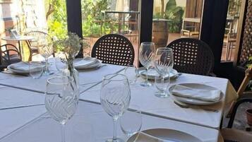 Mesa lista para comer, con platos, vasos y cubiertos, con vistas a un jardín.