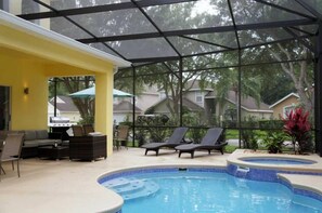 An indoor pool area with lounge chairs, a hot tub, and a covered seating area with a grill.