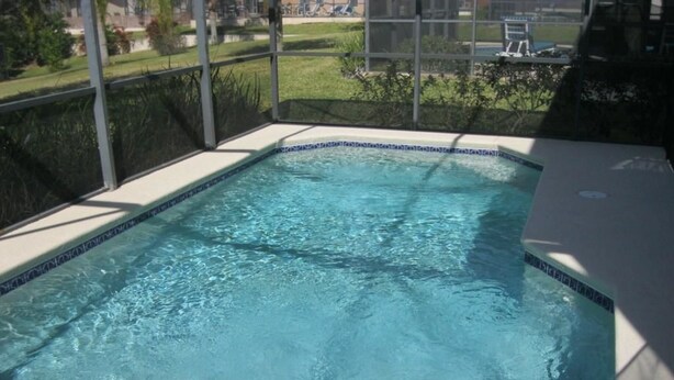 Una piscina rectangular con agua azul cristalina, rodeada por un borde de azulejos y un cerramiento de vidrio.
