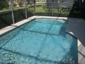 Ein rechteckiger Swimmingpool mit klarem, blauem Wasser, umgeben von einer gefliesten Kante und einer Glaseinfriedung.