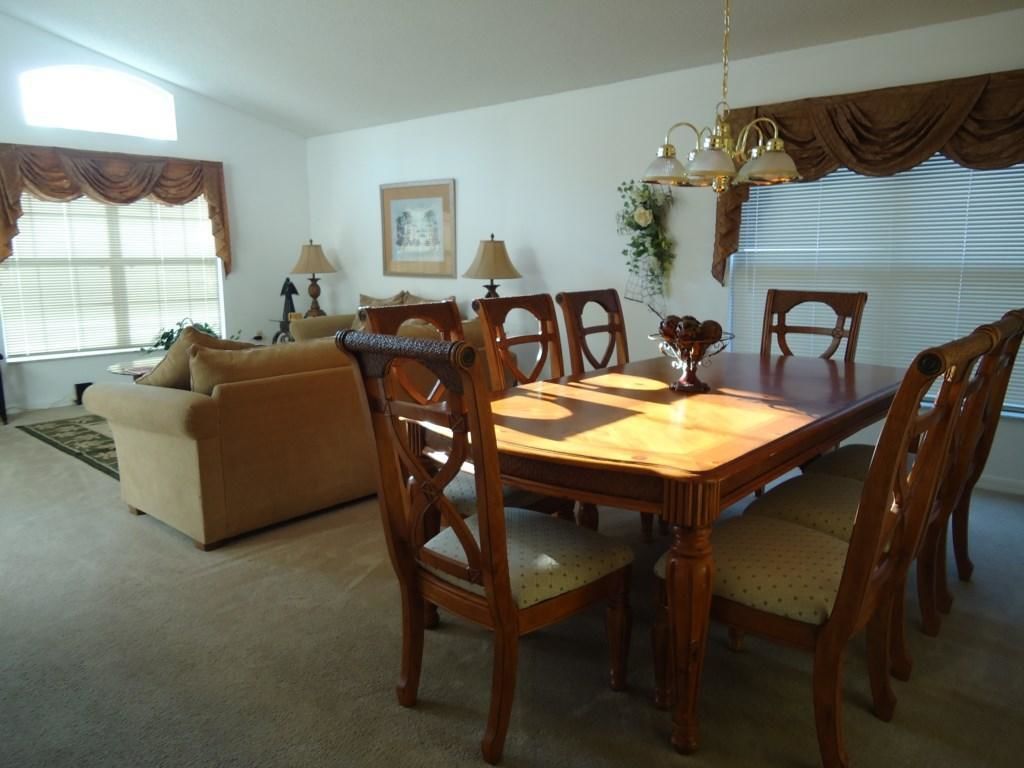 A dining area with a wooden table and chairs, a sofa, and a chandelier.