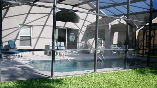 A modern glass-enclosed pool area with lounge chairs and a clear view of the pool. - Brooks Retreat Apartment 4 Bedroom (Haines City)