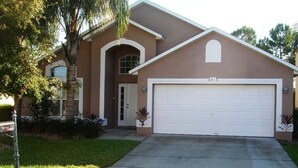 A two-story house with a garage, a front door, and a small porch area. - Brooks Retreat Apartment 4 Bedroom (Haines City)