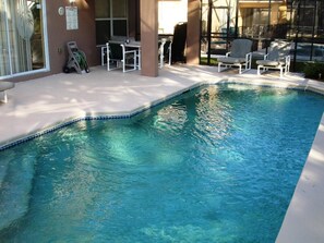 A swimming pool with clear water, surrounded by lounge chairs and a covered seating area.