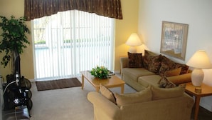 A living room with a beige sofa, two lamps, a coffee table with a plant, and a large window with blinds. - Brooks Retreat Apartment 4 Bedroom (Haines City)