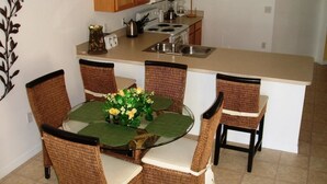 A compact kitchen with a central island, a dining area with wicker chairs, and a microwave above the counter. - Brooks Retreat Apartment 4 Bedroom (Haines City)