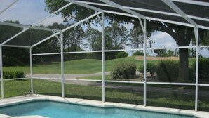 Ein Swimmingpool mit überdachtem Bereich, umgeben von einem weißen Zaun und mit Blick auf einen Golfplatz im Hintergrund.
