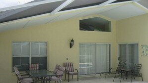Eine Außenpatio mit Tisch und Stühlen, einem überdachten Bereich und einem Fenster mit Jalousien.