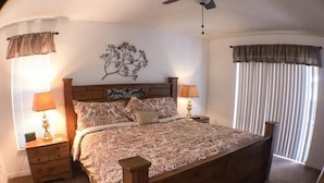 A bedroom with a large bed, two bedside tables with lamps, a ceiling fan, and a window with blinds.
