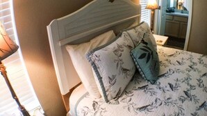 Une chambre à coucher avec un lit, des oreillers, une table de chevet, une lampe et un miroir.