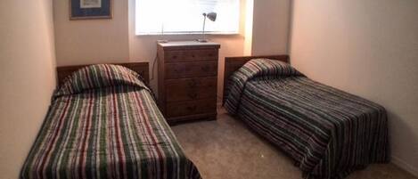 Un dormitorio con dos camas individuales, un aparador, una ventana con persianas y un certificado enmarcado en la pared.