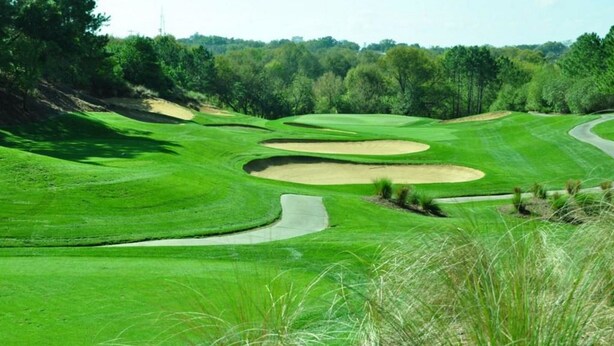 Um campo de golfe com grama bem cuidada, bunkers de areia e um caminho sinuoso.