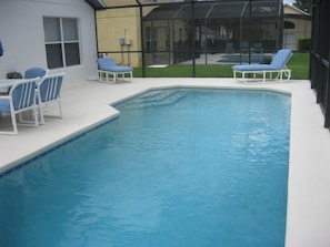 A rectangular swimming pool with two lounge chairs and a table on one side.