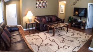 A living room with a brown leather sofa, a patterned rug, a coffee table, a TV, and a small side table with a lamp.