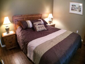 A bedroom with a wooden headboard, a large bed with multiple pillows, two bedside tables with lamps, and a framed picture on the wall.