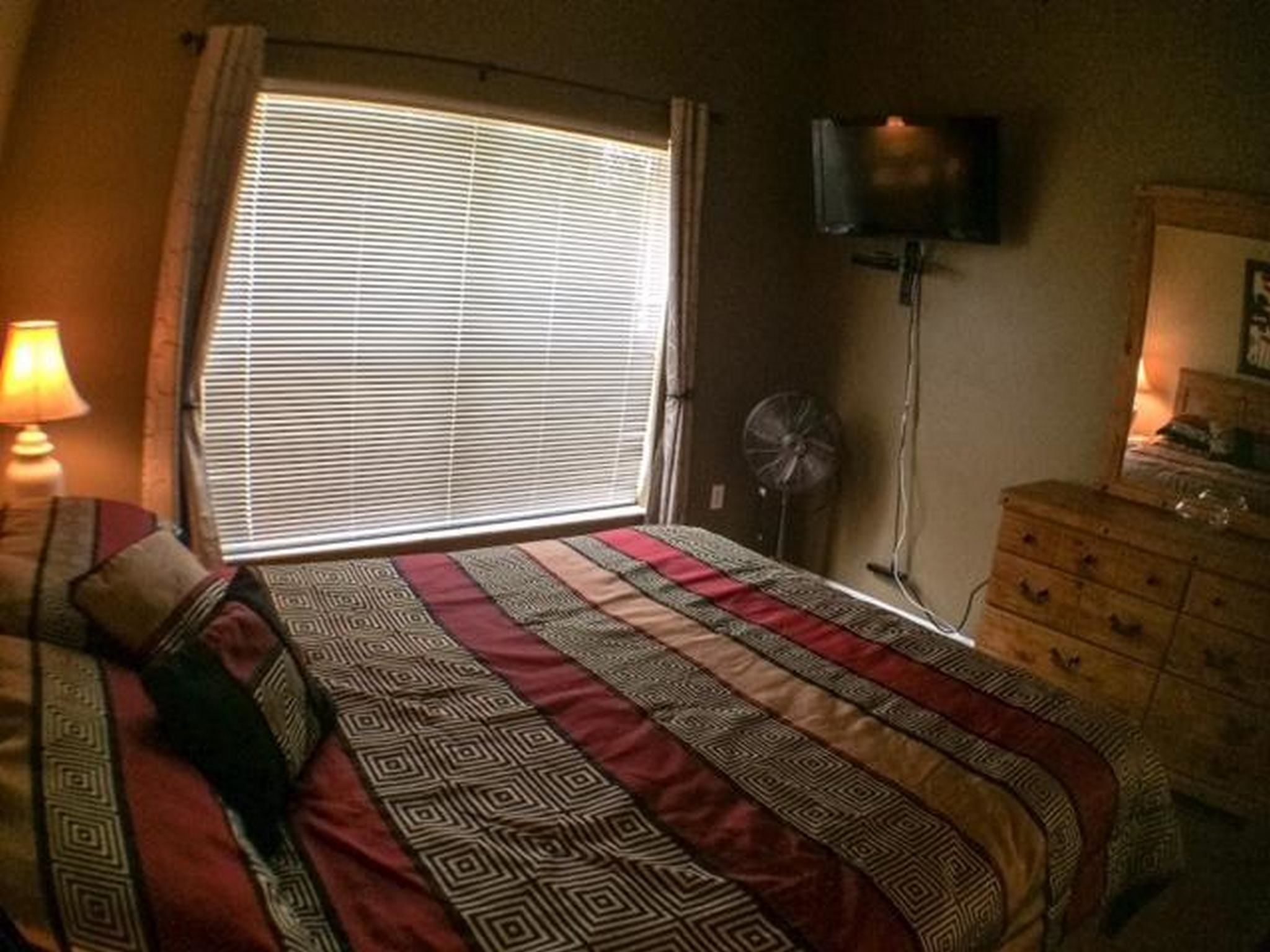 A bedroom with a bed, a dresser, a TV, and a window with blinds.