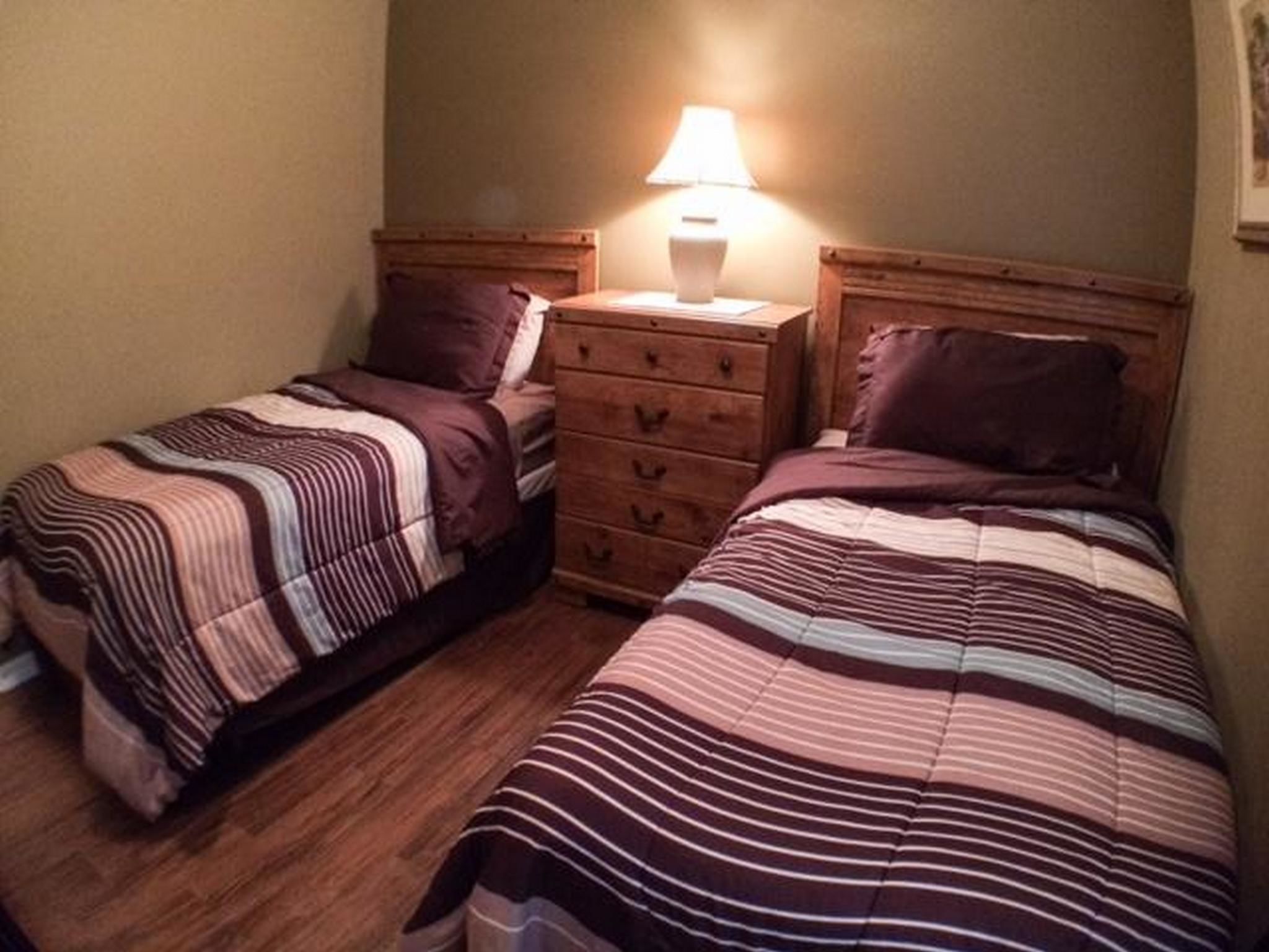 Ein Schlafzimmer mit zwei Einzelbetten, einer hölzernen Kommode und einem Nachttisch mit Lampe.