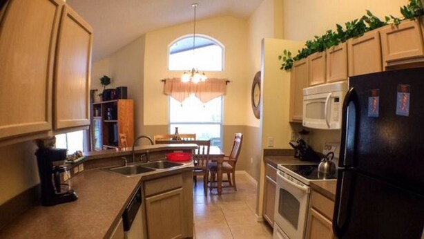 A kitchen with a central island, a dining area with a table and chairs, and a refrigerator. - Clubhouse 1728 Apartment 4 Bedroom (Haines City)