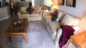 A living room with a beige sofa, a coffee table, and a lamp. There are two paintings on the wall. - Clubhouse 1728 Apartment 4 Bedroom (Haines City)