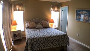 A bedroom with a large bed, two bedside tables with lamps, a door, and a framed picture on the wall. - Clubhouse 1728 Apartment 4 Bedroom (Haines City)