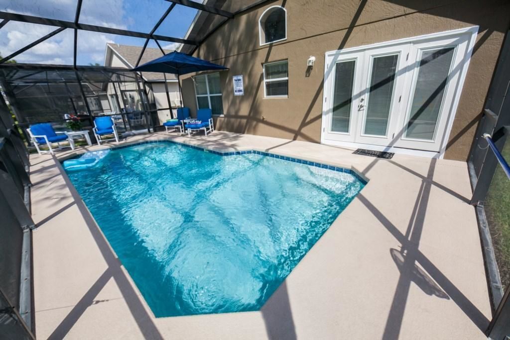 Ein Pool mit blauen Fliesen, umgeben von einer überdachten Terrasse mit blauen Stühlen und Sonnenschirmen.