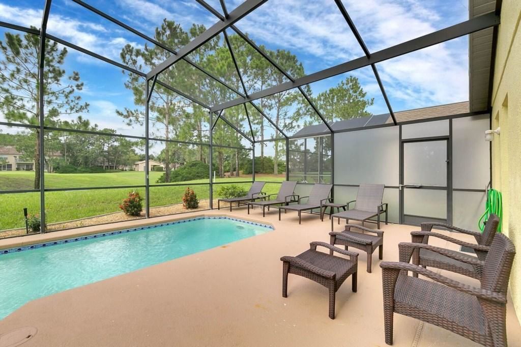A covered outdoor swimming pool area with lounge chairs and a view of a golf course.
