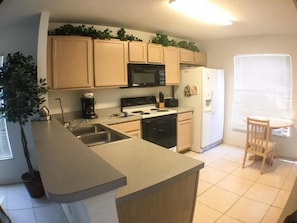 A kitchen with wooden cabinets, a microwave, a stove, and a refrigerator. - St Augustine 2430 Apartment 3 Bedroom (Haines City)