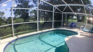 A swimming pool with a glass enclosure, surrounded by lounge chairs and a covered area.