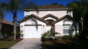 A two-story house with a garage, a covered driveway, and palm trees.