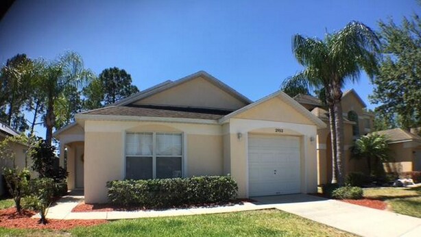 A single-story house with a garage, a front lawn, and a driveway. - Kokomo House Holiday home 3 Bedroom (Haines City)