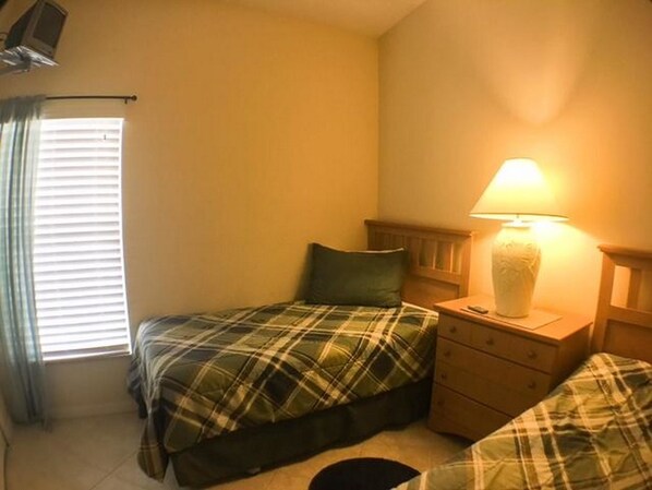 A small, single-bed room with a plaid bedspread, a bedside lamp, and a nightstand.
