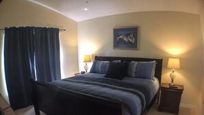 A bedroom with a large bed, two bedside tables with lamps, a painting on the wall, and a window with curtains. - Kokomo House Holiday home 3 Bedroom (Haines City)