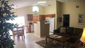 A living room with a black leather sofa, a coffee table, and a dining area with a table and chairs. - Kokomo House Holiday home 3 Bedroom (Haines City)